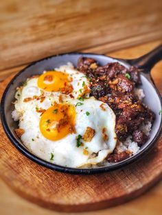 an iron skillet with eggs, meat and rice in it on a wooden cutting board