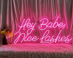 a pink neon sign that says hey babe, me lashes on top of a bed