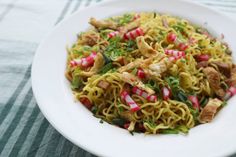 a white bowl filled with noodles and veggies on top of a striped table cloth