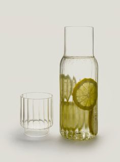 a glass vase filled with lemon slices next to a half empty glass cup on a white surface