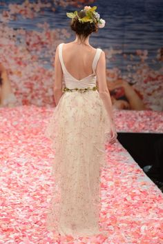 a woman walking down a runway wearing a dress with flowers in it's back