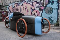 an unusual car is parked in front of a wall with graffitti on it