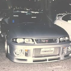 two cars parked next to each other in a parking lot at night with lights on