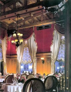 a dining room with tables and chairs covered in white tablecloths, chandeliers and drapes