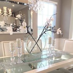 a dining room table with flowers in a vase and candles on the glass tabletop