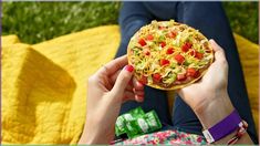 a person is holding up a pizza with noodles and vegetables on it in their hands