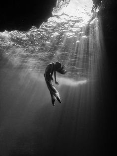 a woman is swimming under the water in black and white