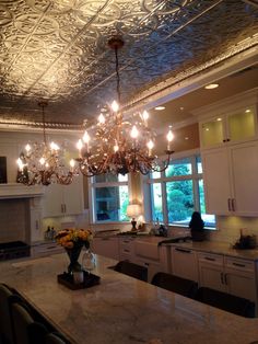 a chandelier hanging from the ceiling in a kitchen with marble counter tops and white cabinets