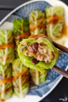 some lettuce with meat and carrots on a blue and white plate next to chopsticks