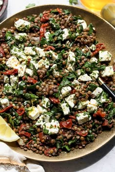 a bowl filled with lentils, feta cheese and lemon wedges on a table