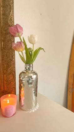 a vase filled with pink and white flowers next to a lit candle on a table