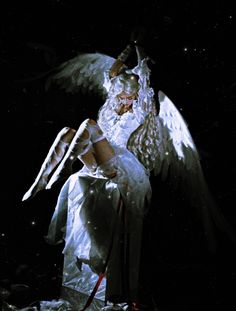 an angel sitting on top of a white chair in the dark with its wings spread