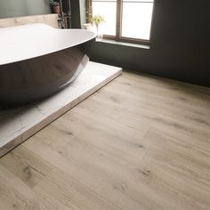 a bathtub sitting on top of a wooden floor next to a window in a bathroom