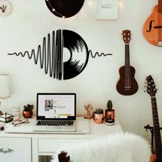 a laptop computer sitting on top of a white desk next to guitars and other musical instruments