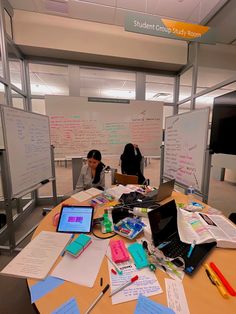 two people sitting at a table with laptops and papers on it, in an office setting