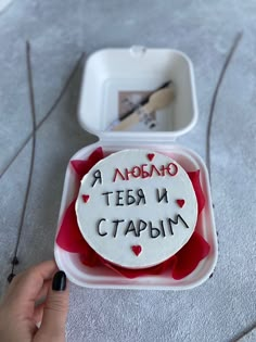 a hand holding a small container with writing on it and some scissors in the background