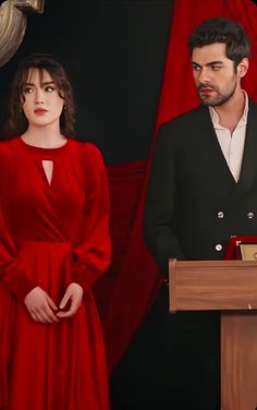 a man and woman standing next to each other in front of a podium with a red curtain behind them