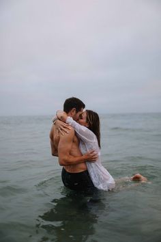 a man and woman in the ocean hugging each other while they are holding each other