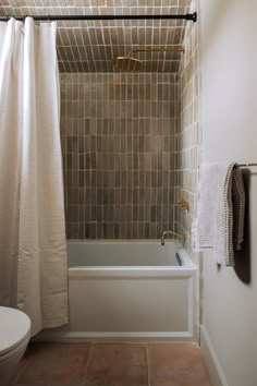 a bath tub sitting under a window next to a toilet and a shower curtain in a bathroom