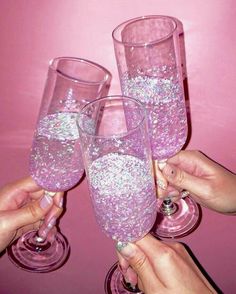 three people holding up wine glasses filled with pink liquid and silver flecks on them