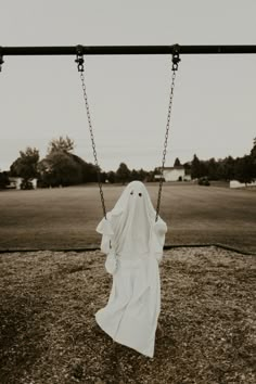 a ghost is sitting on a swing in the grass and wearing a white cloth draped over it's body