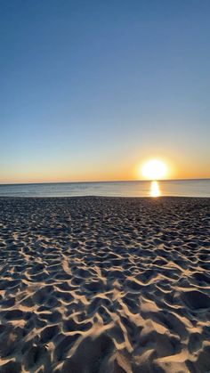 the sun is setting over the beach with sand in front of it and blue sky