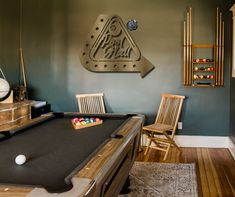 a pool table and chairs in a room with a clock on the wall above it