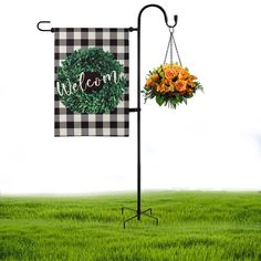 a welcome sign with flowers hanging from it's side on a pole in the grass