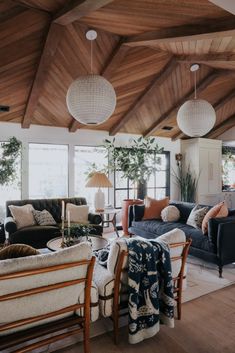 a living room filled with furniture and lots of windows next to a wooden ceiling covered in hanging lights