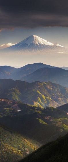 the mountains are covered in green and brown foliage, under a dark sky with clouds