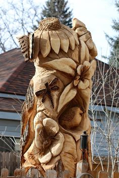 a wooden carving of a man with flowers and a dragonfly on his shoulder, in front of a house