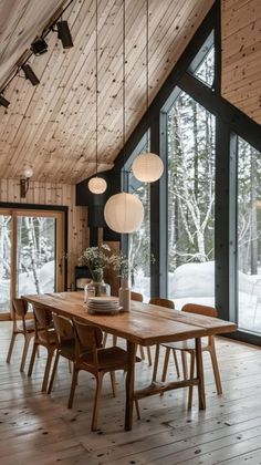 a dining room table with chairs and lights hanging from the ceiling in front of large windows