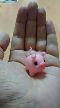 a small pink pig toy sitting in the palm of someone's hand