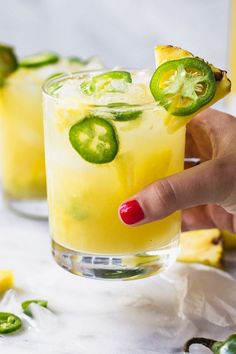 a hand holding a slice of cucumber over a glass filled with lemonade