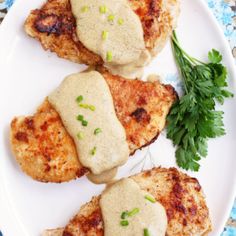 three pieces of chicken covered in gravy on a white plate with parsley