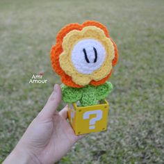 a hand holding a small crocheted flower with question mark on it's center