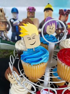 some cupcakes are on a wire rack with paper cutouts in the shape of cartoon characters