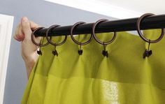 a person is holding up a curtain with rings attached to the rod, and there are other curtains in front of them