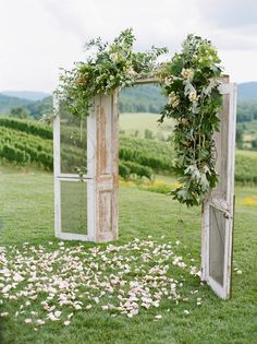 an outdoor ceremony setup with flowers and greenery on the grass in front of two open doors