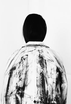 a person standing in front of a white wall wearing a jacket with black stripes on it