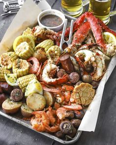 a tray filled with assorted seafood and veggies next to two glasses of beer