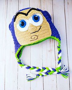 a crocheted hat with blue eyes and braids on the brim is laying on a white wooden surface