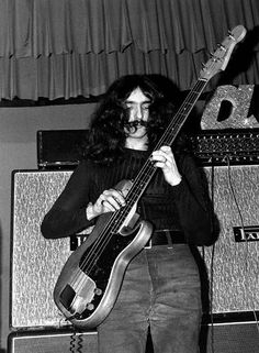 a man with long hair holding a bass in front of two amps and a guitar