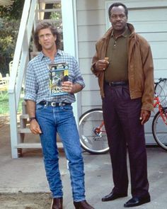 two men standing next to each other in front of a house