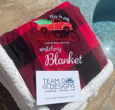 a blanket with a red truck on it next to a swimming pool that says, this is my hallmark christmas movie watching blanket