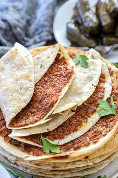 several tortillas stacked on top of each other with sauce and herbs in the background