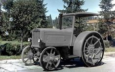 an old fashioned tractor is parked on the side of the road in front of some trees