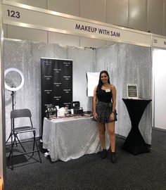 a woman standing in front of a table with makeup on it at a convention or show