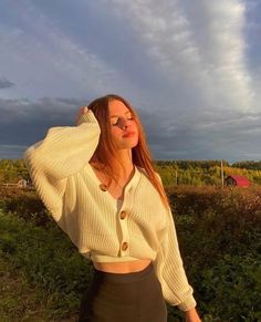 a woman standing in the grass with her hands on her head and wearing a sweater over her shoulders