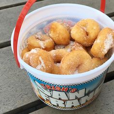 a bucket filled with sugar covered doughnuts on top of a wooden table